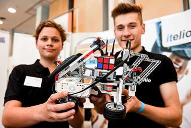 Zwei Auszubildende präsentieren eine selbst gebauten Roboter aus Lego und einem Rubik-Cube auf der Azubimesse 2018.